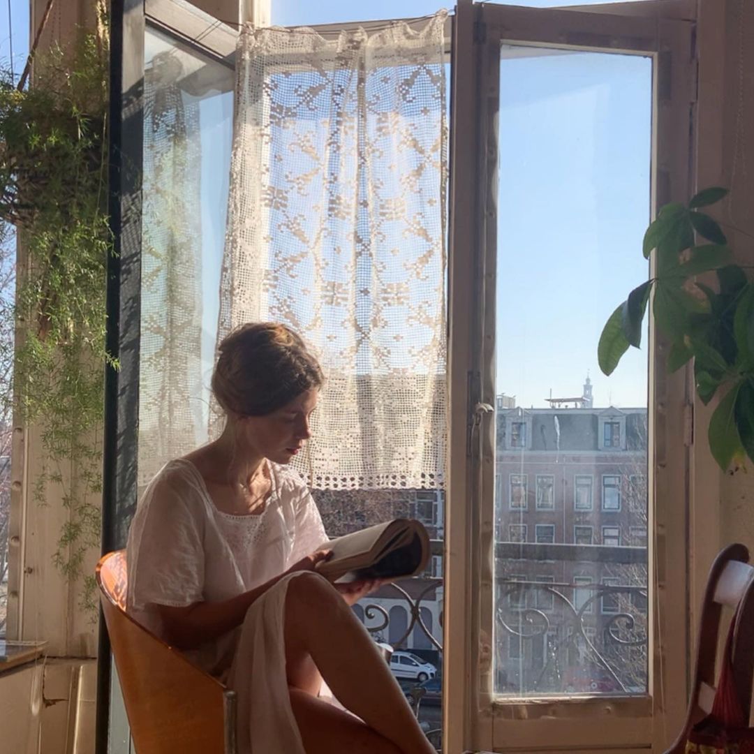 Moça lendo livro e tomando sol na janela